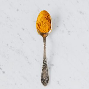 Top view of metal spoon with dry curcuma powder used for healthy gourmet food preparing placed on marble surface